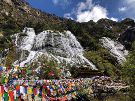 Prayer flags flutter in the wind before the cascading waters of Chumi Gyatse, a sacred waterfall revered by the Monpa people of Arunachal Pradesh, India.